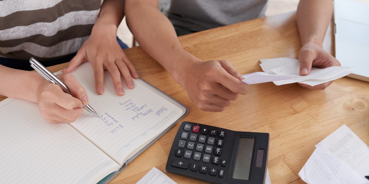 Deux personnes relisent des factures à table, calculatrice et carnet