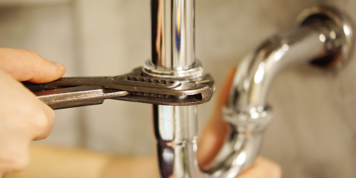 Mains serrant à la clé un siphon chromé sous un lavabo